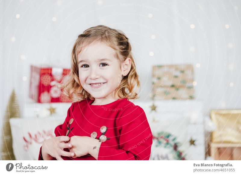 happy cute little girl at home wearing red christmas dress at home over christmas decoration. Holiday concept kid smiling caucasian blonde 3 year old toddler