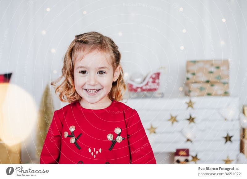 portrait of smiling little girl at home wearing red christmas dress at home over christmas decoration. Holiday concept happy kid caucasian blonde 3 year old