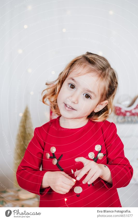 portrait of cute little girl at home wearing red christmas dress at home over christmas decoration. Holiday concept happy kid smiling caucasian blonde