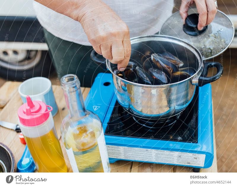 Senior woman cooking mussels in camping gas on in her van 60s adventure aged alternative black camper campsite can caravan elderly female food freedom happiness