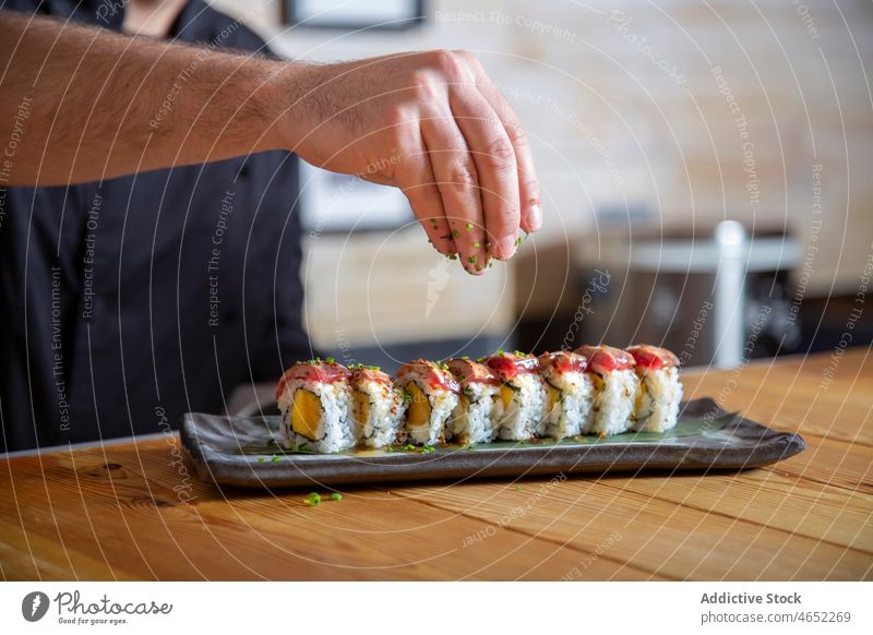 Anonymous man sprinkling herbs on sushi rolls chef tuna japanese sprinkle asian food serve seafood culinary cuisine tasty fresh plate set restaurant oriental