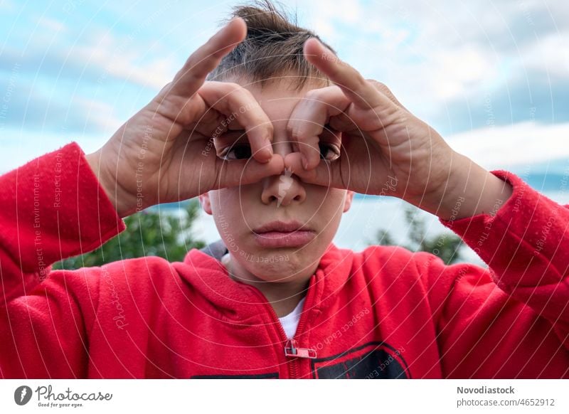 Portrait of a 9 year old boy outdoors, with his hands aroung his eyes, like he's using binoculars, wearing casual clothes gesture expression portrait caucasian
