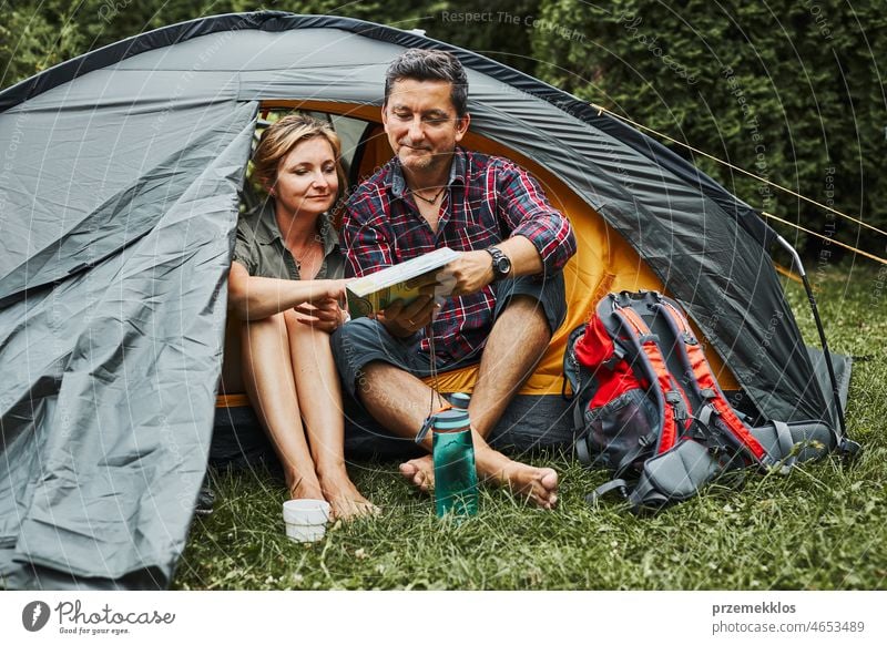 Happy couple relaxing in tent at camping during summer vacation. Man and woman planning next trip looking at map. Actively spending vacations outdoors close to nature