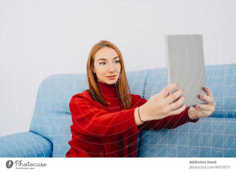 Woman on sofa taking selfie on tablet woman self portrait using couch lounge chill comfort rest redhead take photo memory shoot female sit red hair relax moment