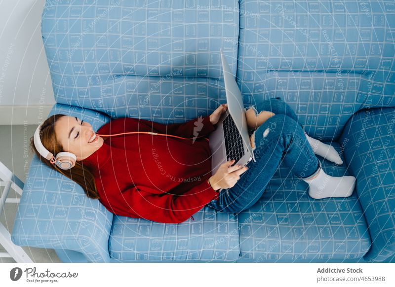 Relaxed woman with laptop and headphones using online at home internet relax weekend free time female browsing watch rest surfing netbook smile sofa connection