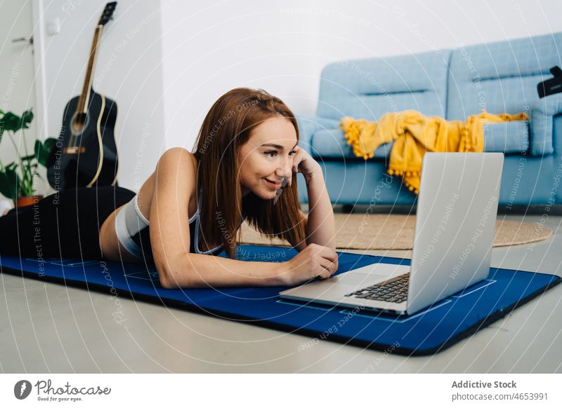 Smiling woman lying on mat with laptop practice using yoga online fitness watch video tutorial female netbook young smile internet training sportswear relax