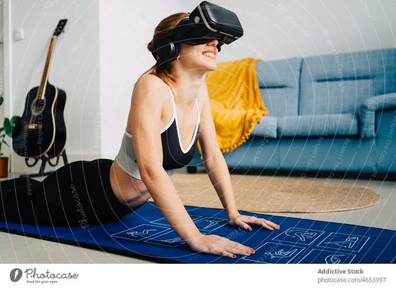 Smiling woman in VR glasses practicing yoga vr practice using virtual reality goggles cobra pose bhujangasana female sportswear headset online mat internet