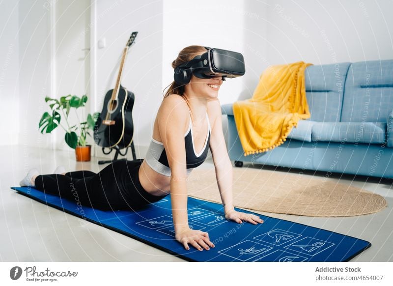 Smiling woman in VR glasses practicing yoga vr practice using virtual reality goggles cobra pose bhujangasana female sportswear headset online mat internet