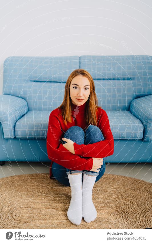 Female embracing knees while sitting near sofa woman couch carpet shy rest lonely redhead unsure female comfort red hair relax cozy calm appearance living room