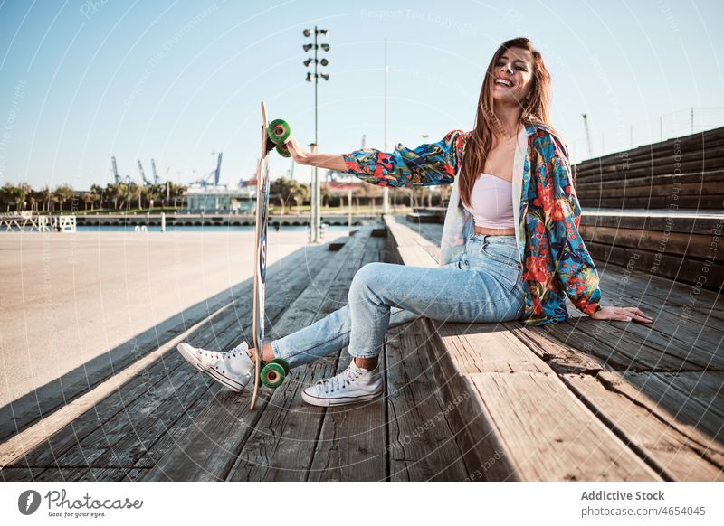 Young happy trendy female with longboard woman style city urban relax summer chill appearance outfit young skater cool confident slim millennial blue sky jeans