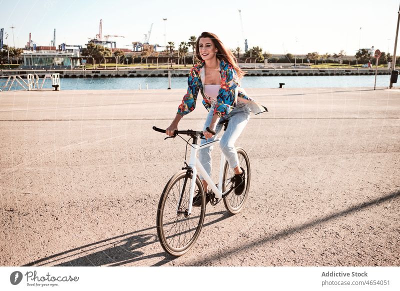 Smiling woman riding bicycle on embankment river city park activity summer weekend hobby female ride leisure cheerful carefree young smile enjoy street happy