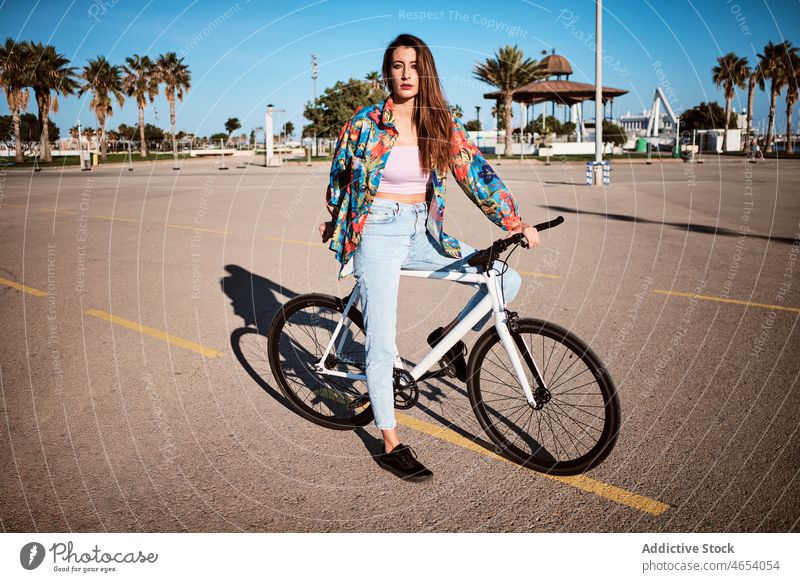 Woman riding bicycle on pavement woman park activity summer weekend hobby female ride leisure carefree young blue sky enjoy street free time trees relax lady