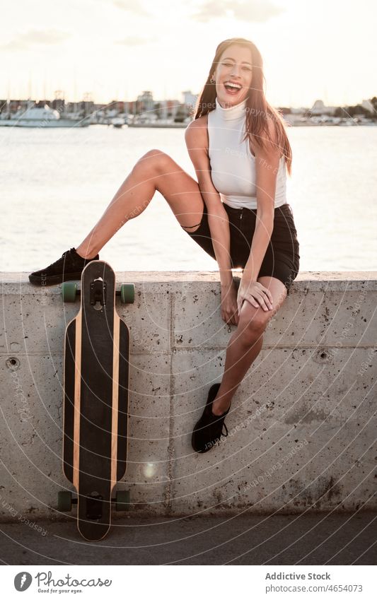 Smiling woman with longboard on embankment sea summer style relax weekend leisure appearance female cheerful slim seashore smile young trendy skater happy water