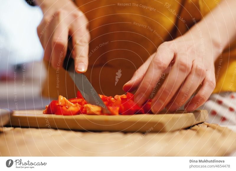 Woman chopping red bell pepper on wooden cutting board, cooking healthy meal for dinner. Chef making salad of fresh vegetables. food kitchen tomato natural