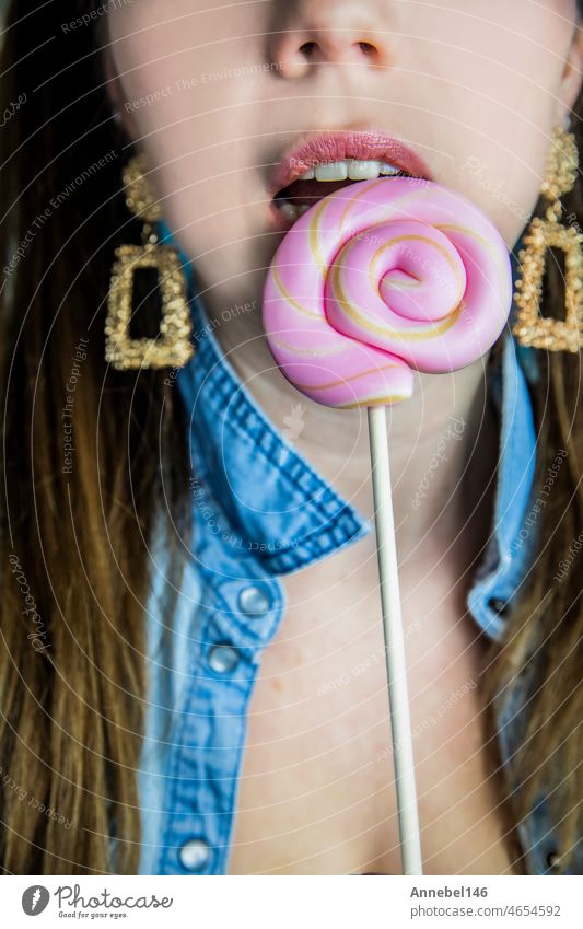Portrait of a beautiful girl with colorful pink twirl lollipop hard candy on blue background, sweets,sugar and unhealthy food concept woman lolly fashion face