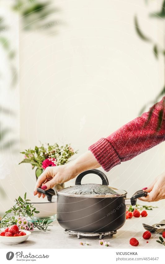 Woman hands holding black cooking pot on kitchen table woman raspberries light wall background home front view porridge flower flower bouquet food homemade