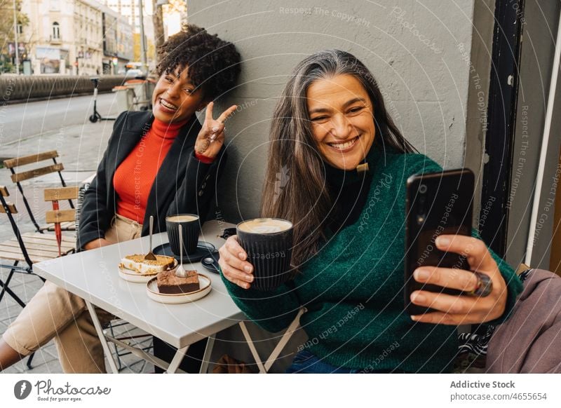 Hispanic woman taking selfie with black friend in cafe women laugh using smartphone coffee latte gesture peace happy female moment positive together girlfriend