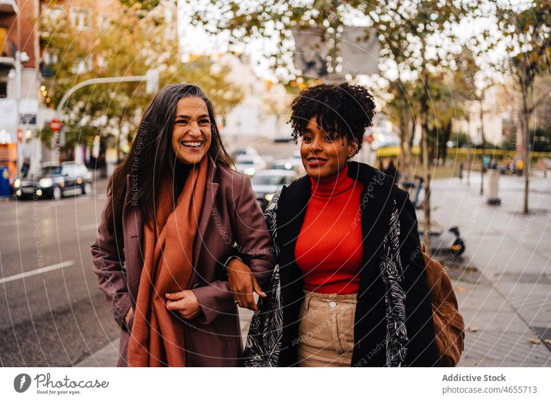 Smiling women walking on city street pedestrian friend together glad roadside urban pavement commute female multiethnic delight happy talk african american