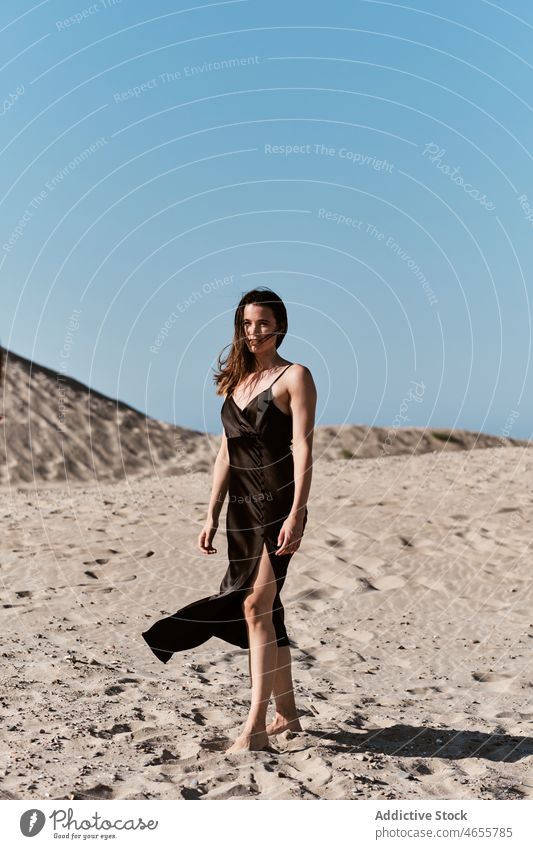 Slim attractive woman standing on sandy beach in sunny day desert summer cloudless blue sky barefoot dress harmony sundress daytime travel rest relax nature