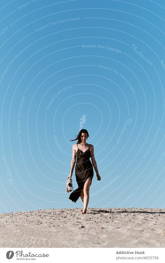 Slim attractive woman walking on sandy beach in sunny day desert summer cloudless blue sky barefoot dress harmony sundress daytime travel rest relax nature