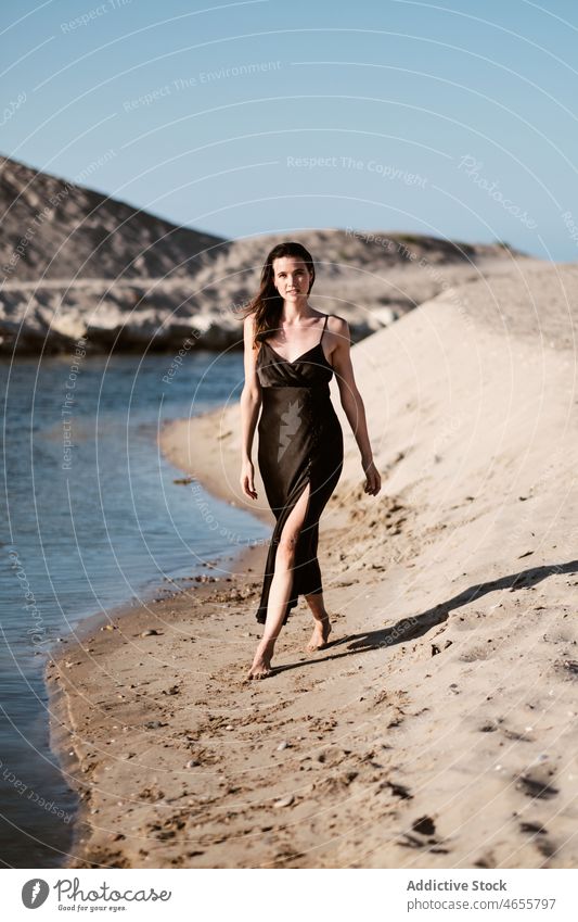 Slim attractive woman standing on sandy beach in sunny day desert summer cloudless seashore blue sky barefoot seaside dress harmony sundress coast travel rest