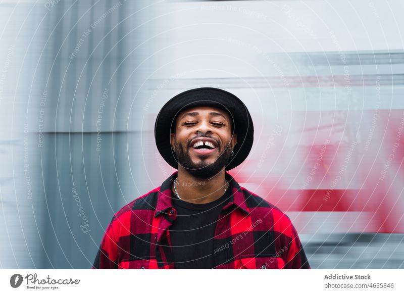 Happy ethnic man on blurred street cheerful hat smile appearance laugh glad personality style portrait male positive individuality joy happy beard optimist guy