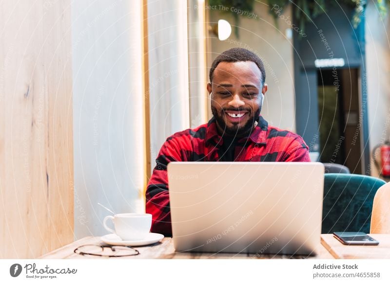 Smiling black man working on laptop in cafe earphones using online internet browsing freelance male african american netbook surfing coffee remote connection