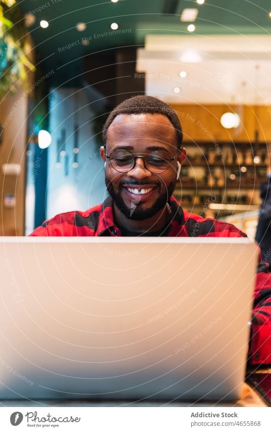Smiling black man working on laptop in cafe earphones using online internet browsing freelance male african american netbook surfing remote connection relax