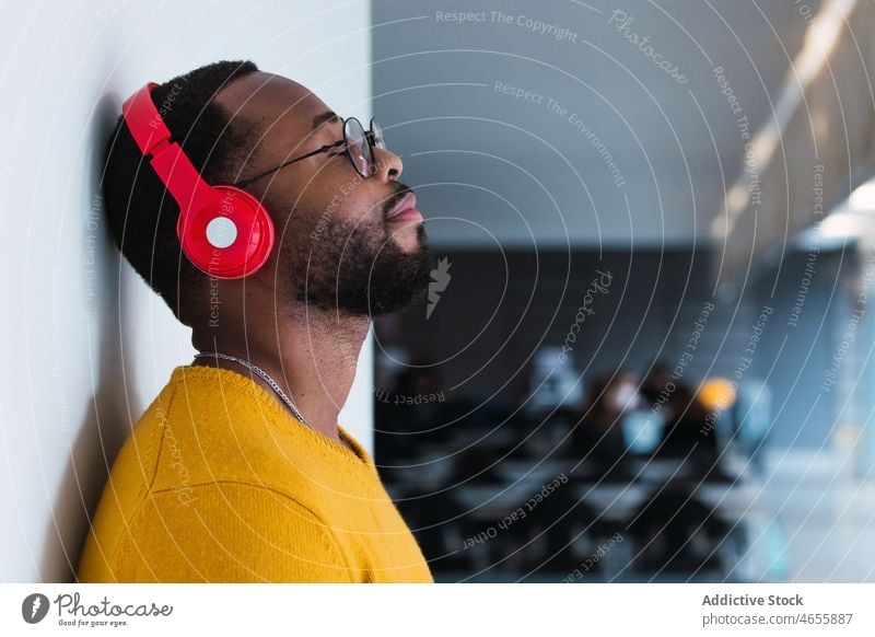 Black man listening to music in headphones using relax rest chill song meloman male black african american enjoy device wireless eyes closed eyeglasses playlist