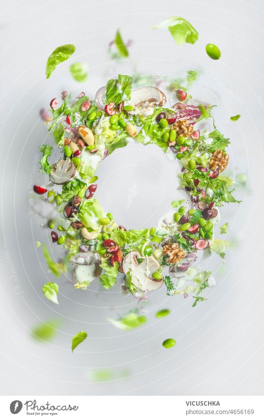 Circle frame of flying healthy green salad. Balanced vegan food with copy space. Levitation of food circle lettuce nuts beans dressing vegetables balanced