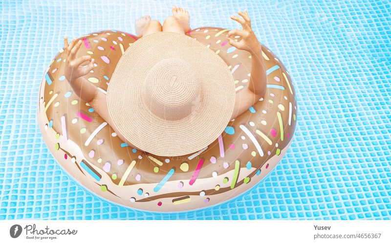 Beautiful girl in the in blue swimming pool. Pretty teenager in a straw hat with inflatable donut. Summer vacation concept. Back view. Summer vacation concept. WEB banner format. Copy space