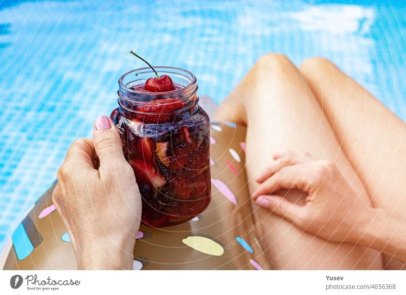Beautiful women in the in blue swimming pool. A woman's graceful hand holds a berry cocktail. Inflatable donut. Close-up. Summer vacation stock photo. Back view.