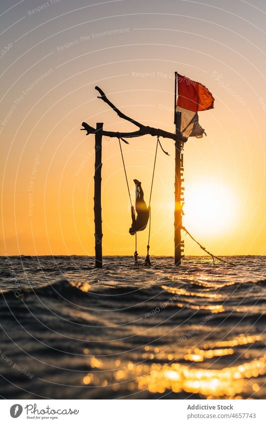 Silhouette of person hanging on swing in sea silhouette tourist tropical exotic sunset vacation nature sundown upside down water scenic traveler ripple sunlight