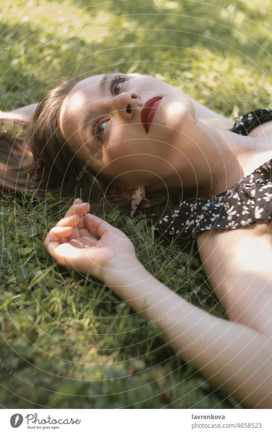 Young woman in black dress lying on green grass caucasian portrait meadow nature above adult daydreaming female garden girl hands happy leisure lifestyle
