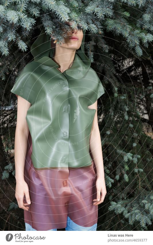 A girl dressed in a latex raincoat is hiding in these bushes. Pine trees with green branches fit her perfectly in this image. A fashion model shows the best qualities of latex in a different way.
