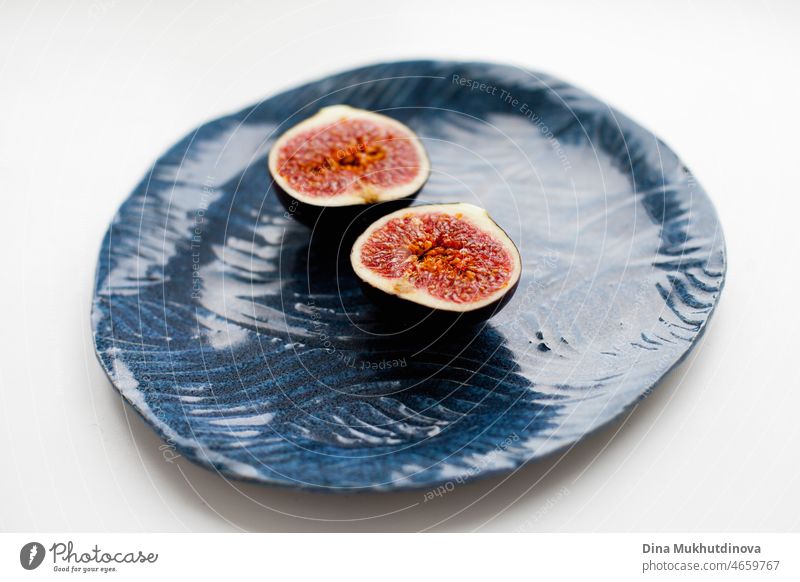 A ripe fig cut in half on a blue artisanal plate on white table. Delicious ripe fig fruit as dessert for healthy eating. natural tropical food background diet