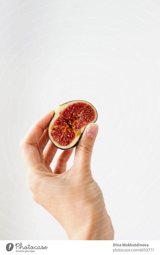 Hand holding a ripe half of fig fruit isolated on white background with copy space on top and right. Vertical image of fig, femininity and sensuality concept.