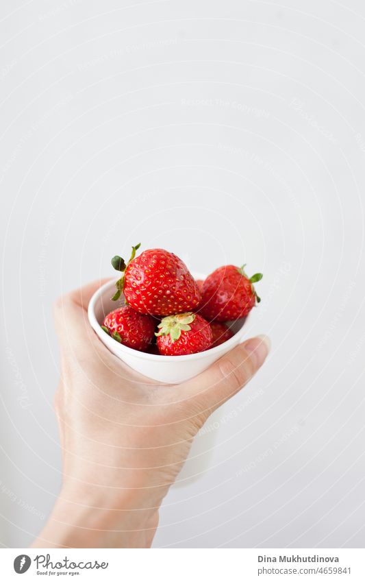 Hand holding a white paper cup with fresh ripe strawberries on white background. Strawberries in cup and copy space on top. strawberry breakfast snack natural