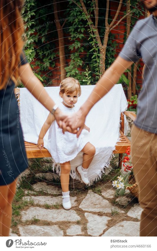 Young parents holding hands with their little jealous serious daughter in the background in the garden. Love and family concept. protection fingers safety daddy