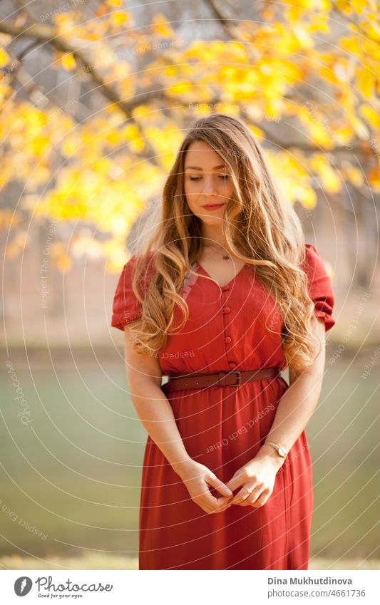 beautiful woman with long in red dress walking in the forest by the lake among trees. Romantic walk in the woods in autumn nature on autumn leaves. adult