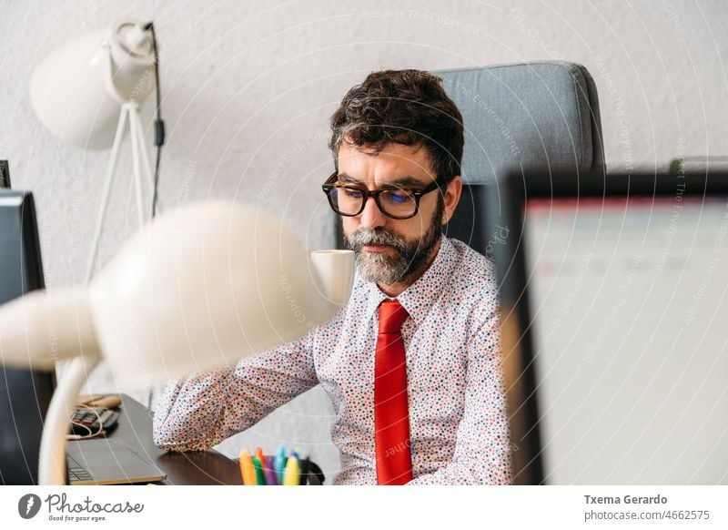Middle-aged businessman with beard and glasses having coffee in office designer studio necktie pc computer desk agency creativity entrepreneur lifestyles