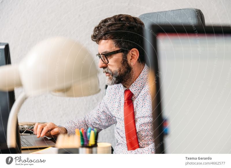 Middle-aged businessman with beard and glasses concentrating with his work in front of his computer concentration office designer studio necktie pc desk agency