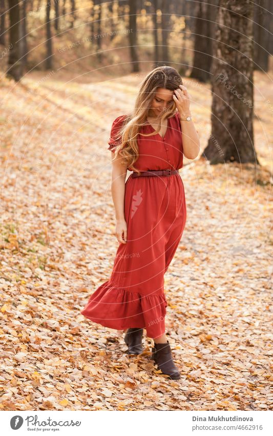 beautiful woman with long in red dress walking in the forest among trees. Romantic walk in the woods in autumn nature on autumn leaves. adult elegance fall