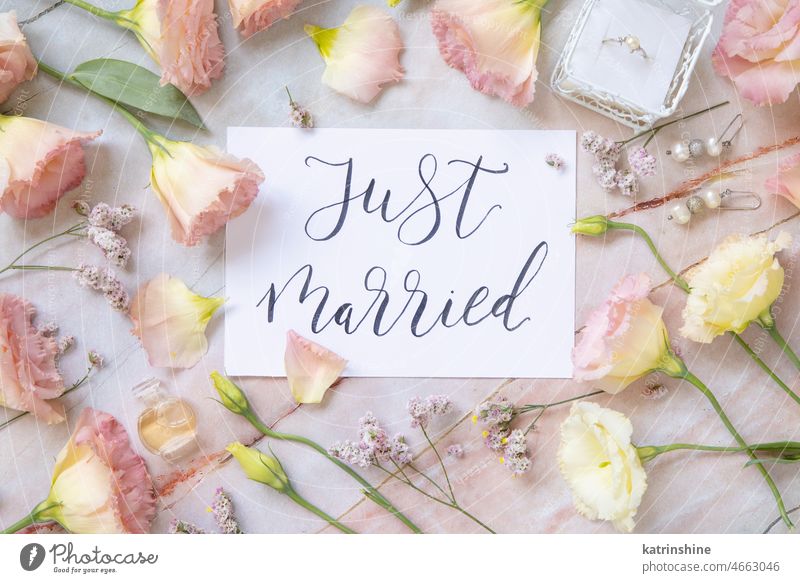 Card with the text JUST MARRIED surrounded by pink flowers Wedding card handwritten Flowers top view Marble table paper quote Marriage lettering message