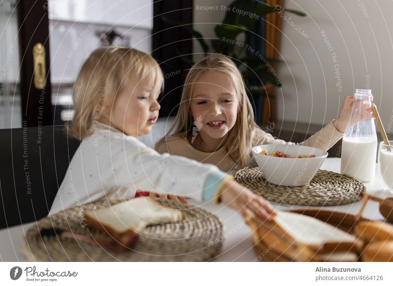 Cute caucasian siblings sitting at table on kitchen early morning and preparing breakfast with colorful cornflakes and milk. Kids enjoying life with healthful food, healthy lifestyle concept