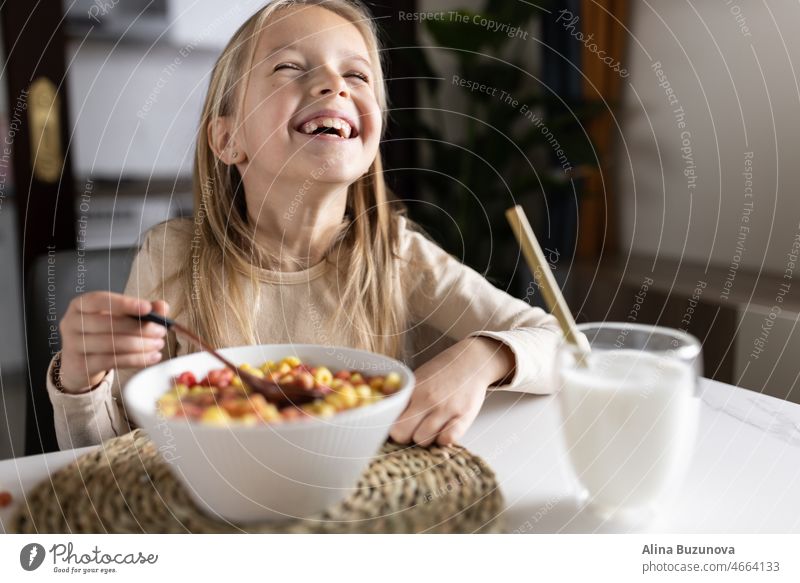 Cute little caucasian girl sitting at table on kitchen early morning and preparing breakfast with colorful cornflakes and milk. Kid enjoying life with healthful food, healthy lifestyle concept