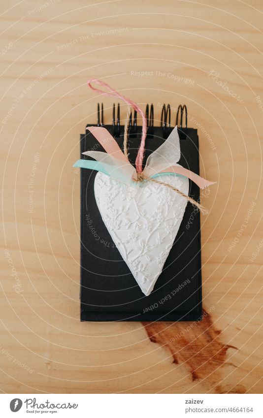 notebook with black sheets on a wooden table with a white heart. paper mock up copy space background workspace nobody flat lay day writing wedding valentine