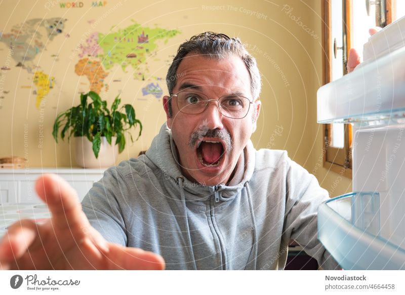 Portrait of a 45 year old man by the fridge door looking shocked, wearing glasses and casual outfit middle aged caucasian mustache moustache specs face portrait