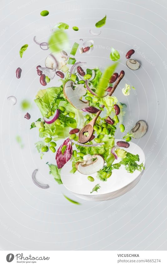 Healthy green salad flying  over white bowl. healthy floating at white mushrooms kidney beans edamame onion wall background flying food concept without