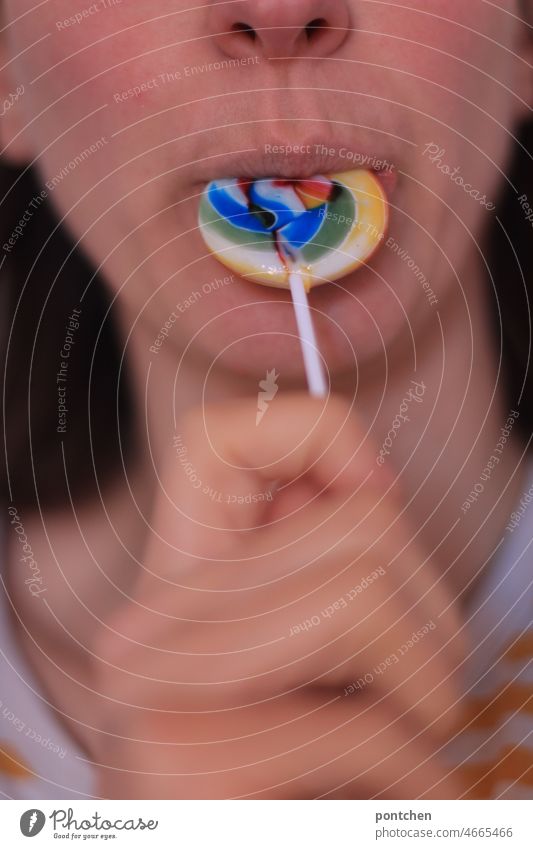 A woman sucks a colorful, round lollipop in rainbow colors with pleasure and revels in childhood memories Lick variegated Woman Mouth candy calories